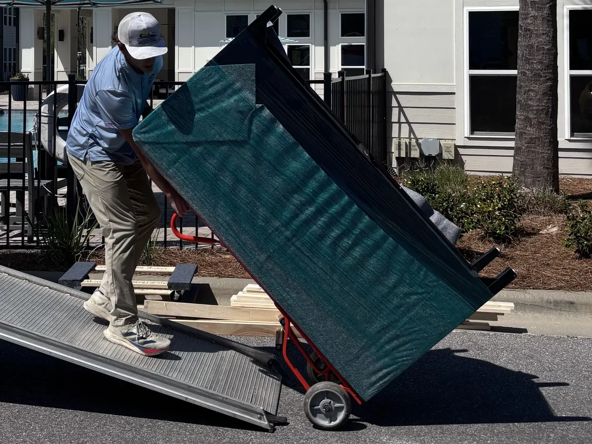 Southern Shores Moving mover wheeling a shrink-wrapped dresser up a truck ramp on a hand truck during a move in Navarre, Florida